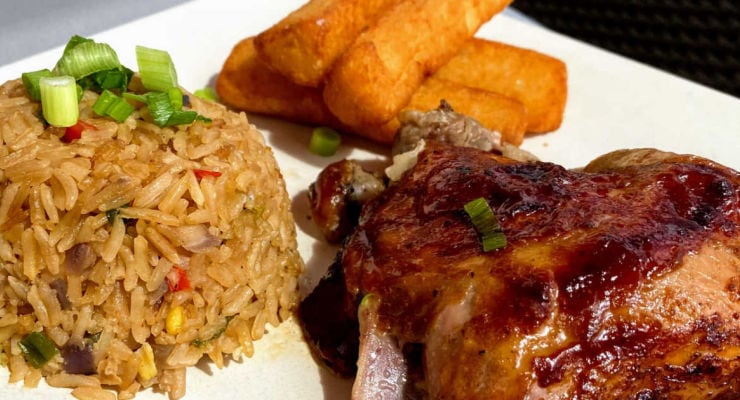 A plate of food featuring a serving of fried rice garnished with chopped green onions, crispy golden fries, and a piece of glazed roasted chicken with green onion topping.