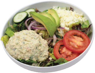 A white bowl filled with a salad featuring sliced tomatoes, avocado, cucumber, red onion, crumbled cheese, mixed greens, and a scoop of tuna or chicken salad.